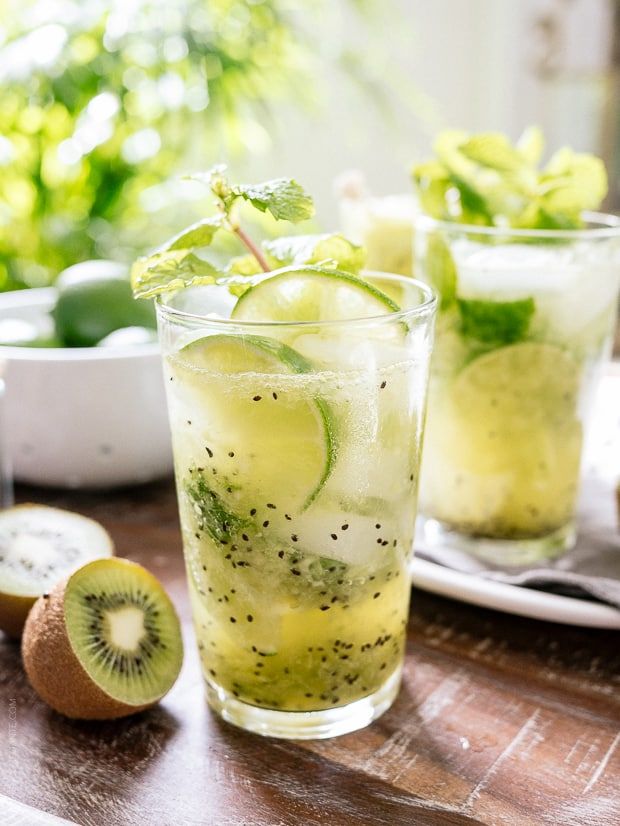 two glasses filled with lemonade and kiwi slices on top of a wooden table