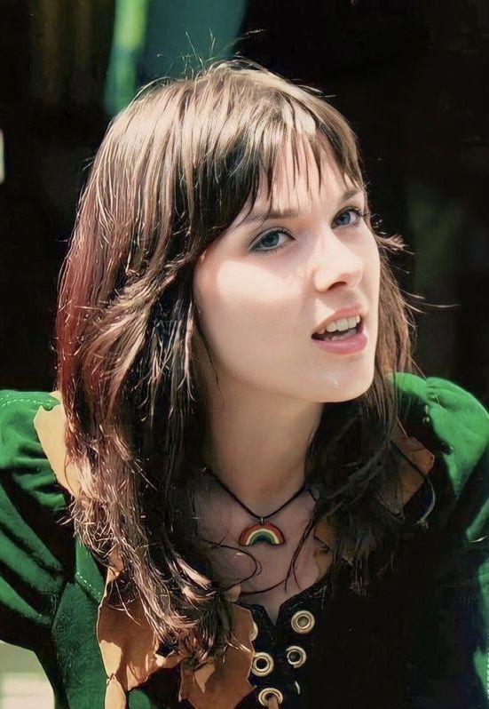 a woman with long hair wearing a green shirt and black necklace looking off to the side