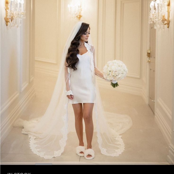 a woman in a white wedding dress holding a bouquet and standing next to a chandelier