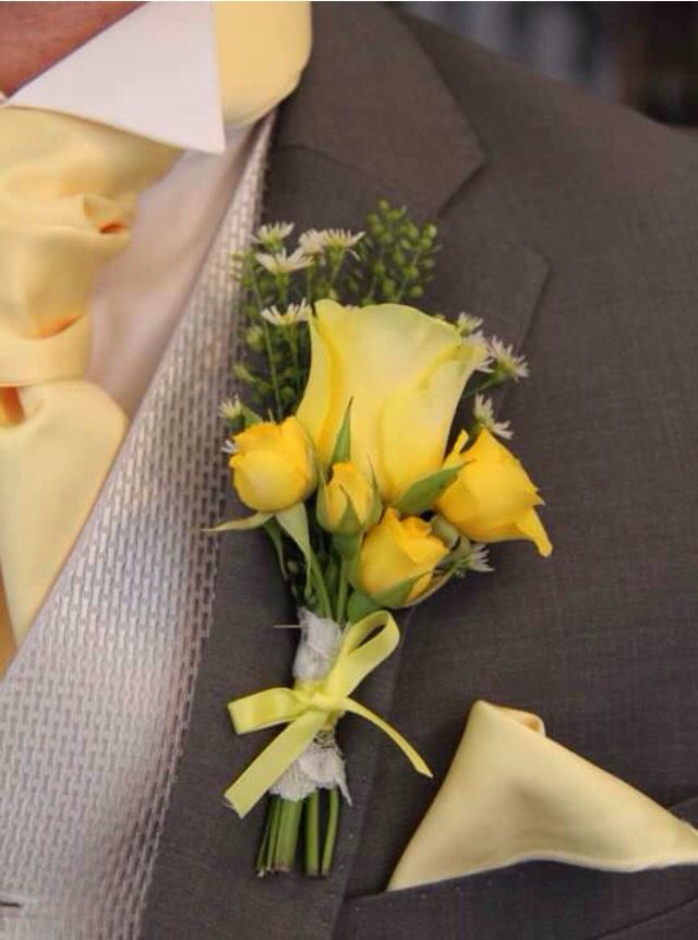 a boutonniere with yellow roses and greenery attached to the lapel