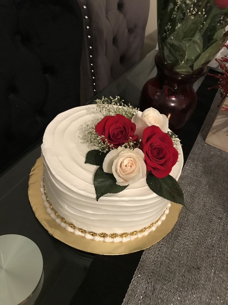 a cake with white frosting and red roses on top is sitting on a table