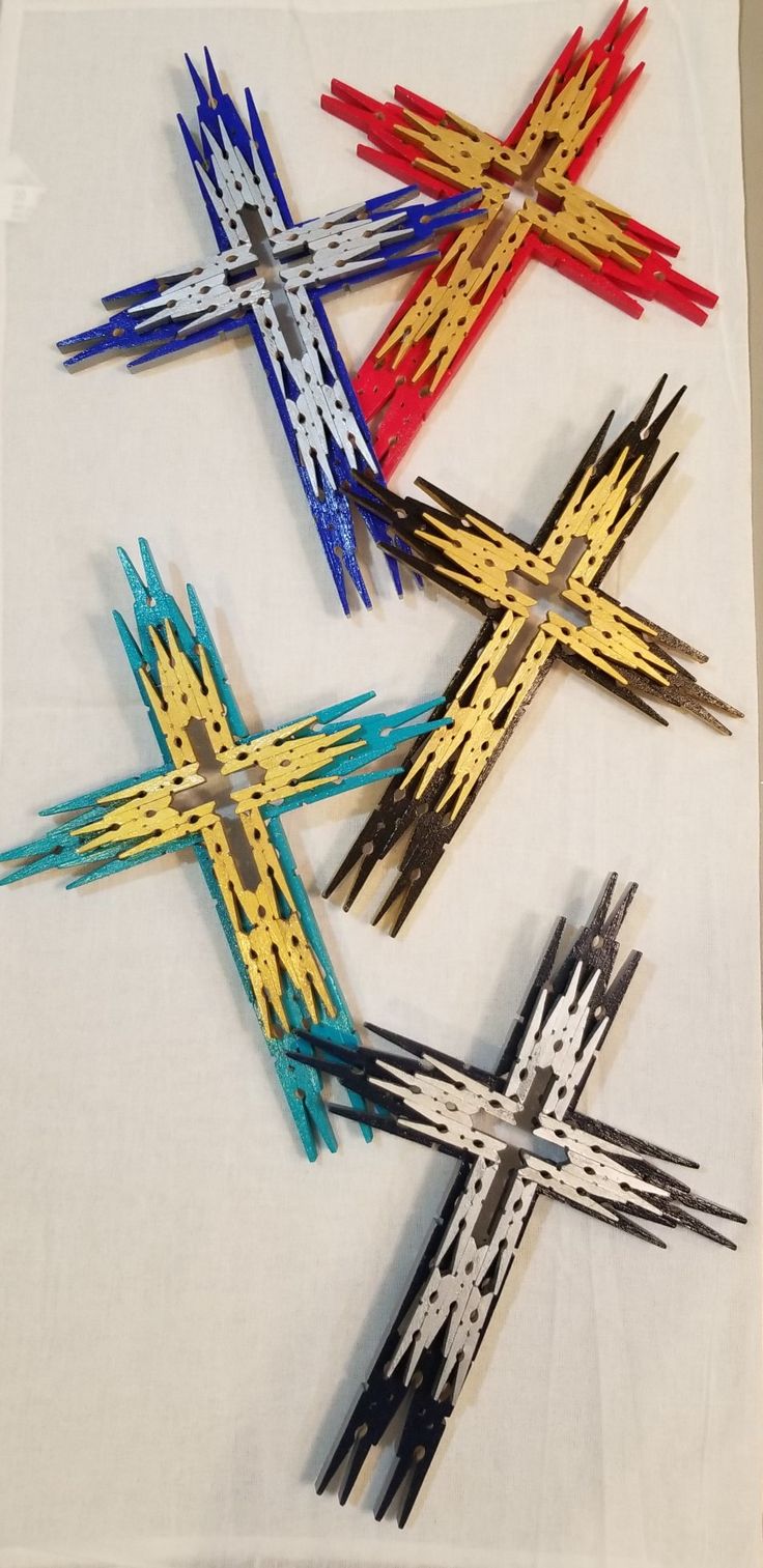 four wooden crosses on a white cloth with red, yellow and blue sticks sticking out of them