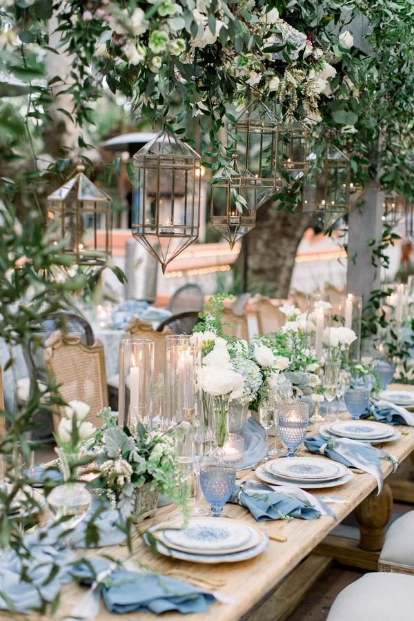 an outdoor table set with blue and white plates, place settings and greenery on the tables