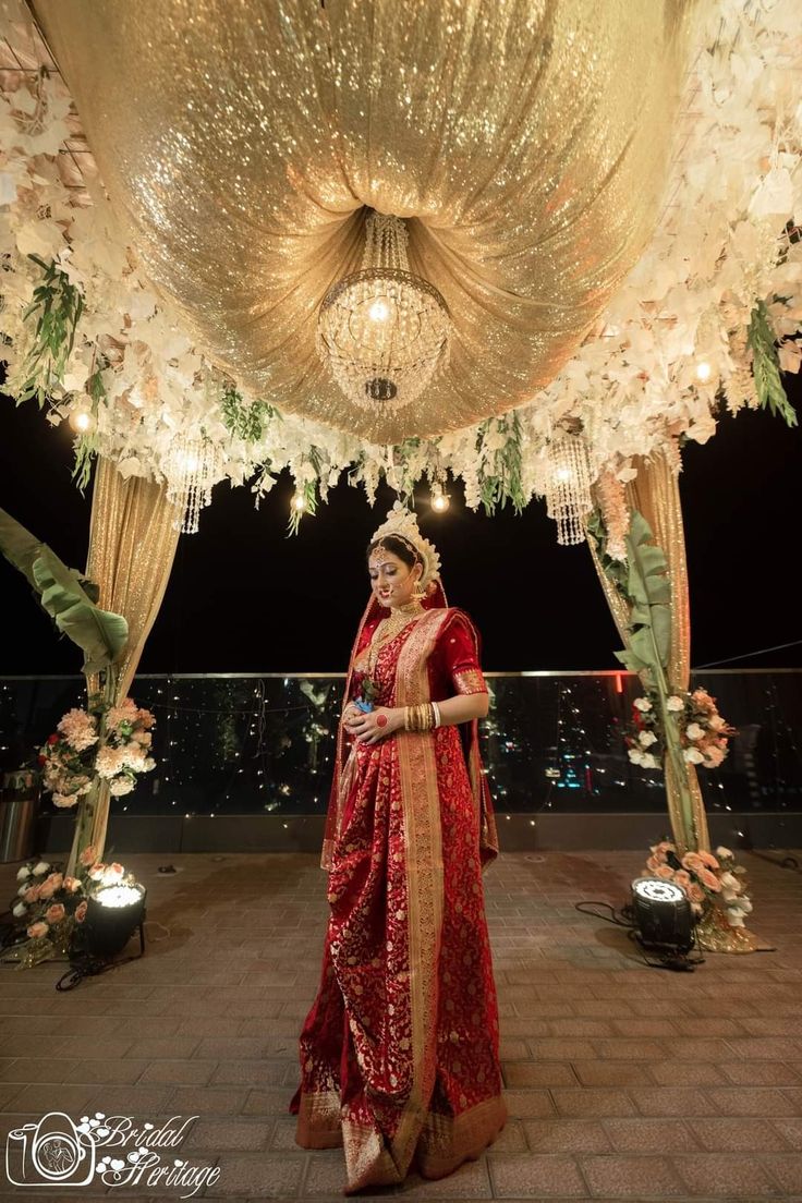 a woman in a red and gold sari standing under a chandelier