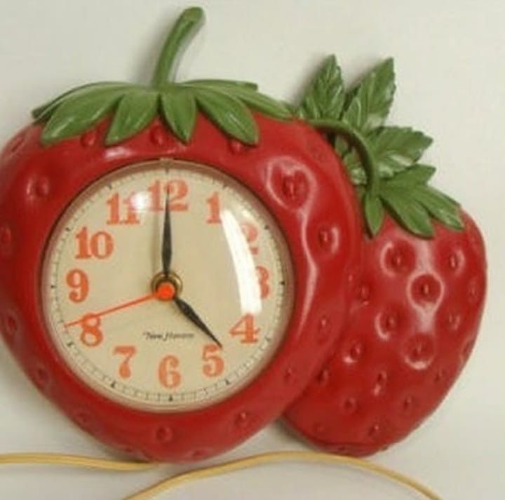 a red clock sitting on top of a white wall next to a strawberries design