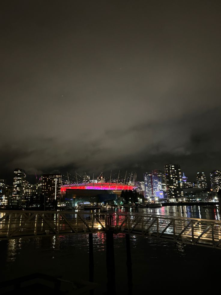 the city skyline is lit up at night with bright lights and clouds in the sky