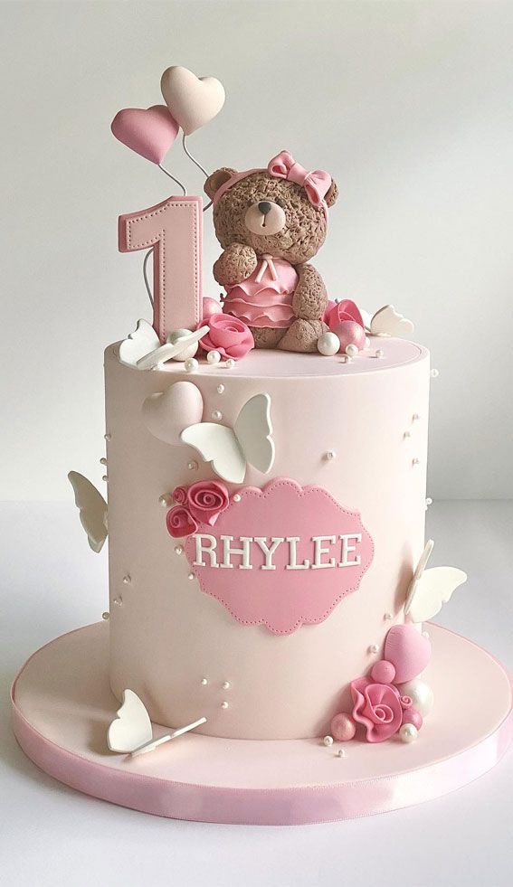 a pink and white cake with a teddy bear on top