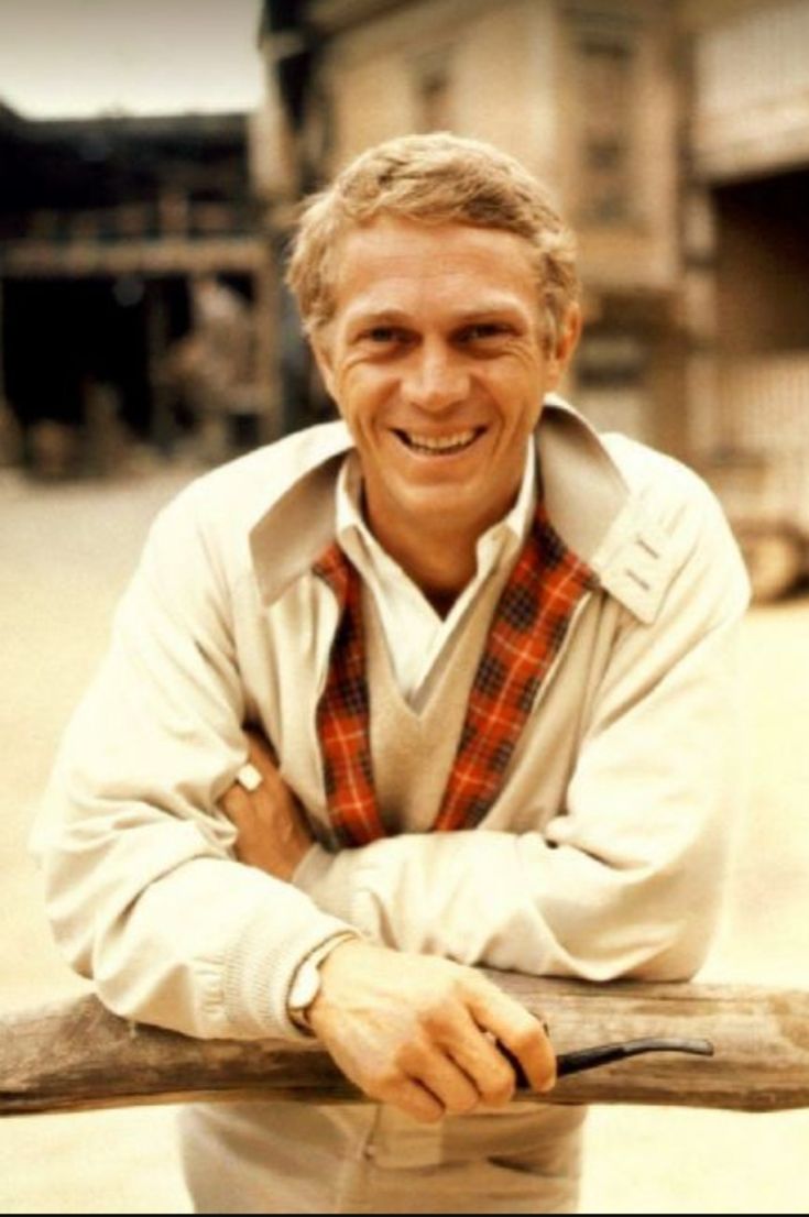 a man leaning on a wooden fence with his arms crossed and looking at the camera