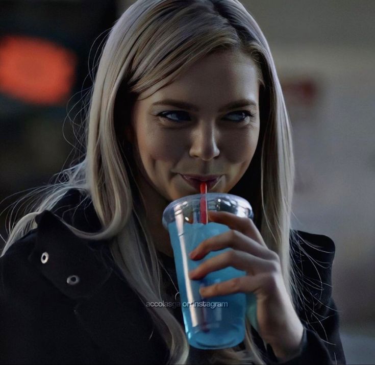 a blonde haired woman drinking from a blue plastic cup with a straw in her mouth