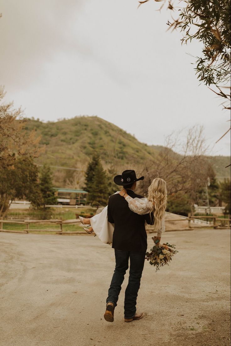 a man carrying a woman on his back in the middle of a dirt road with mountains in the background