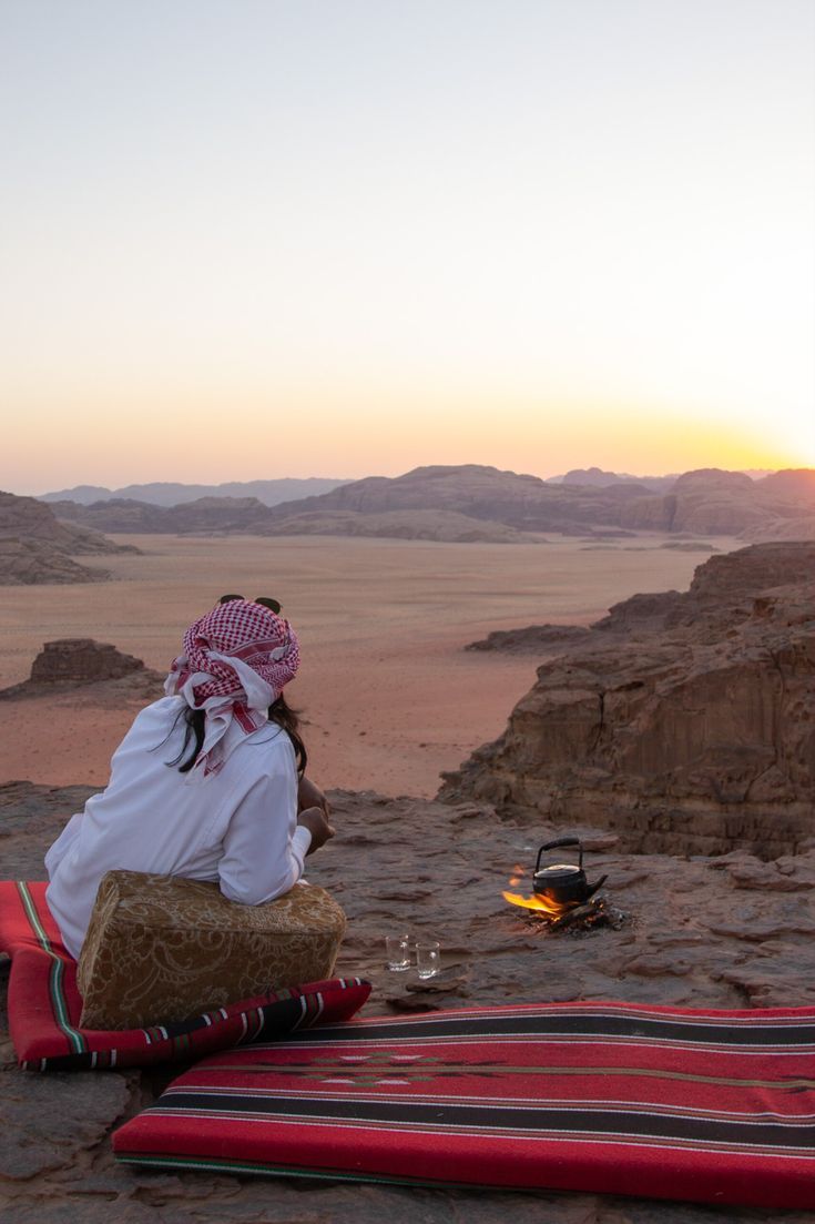 a woman sitting on top of a blanket in the desert