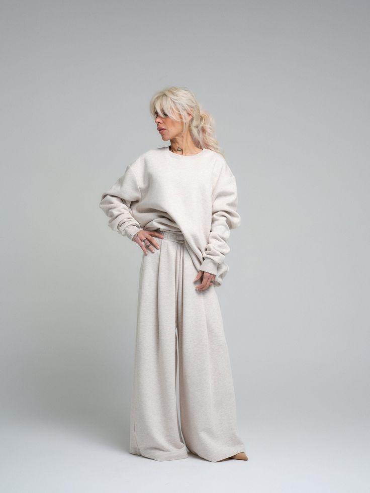 Find your comfort zone in our ecru loungewear set, a perfect marriage of style and relaxation. This ensemble, made from a cotton and polyester blend, provides both the softness of cotton and the durability of polyester. The set includes a relaxed-fit sweatshirt and coordinating wide-leg pants, both designed to offer you a luxurious feel and a chic, understated look. FEATURES: Oversized sweatshirt with drop shoulders for a modern silhouette. High-rise with a wide-leg cut to complement the relaxed Relaxed Fit Beige Sweatpants With Ribbed Cuffs, Relaxed Fit Off White Bottoms For Loungewear, Cozy Cream Sweatpants For Loungewear, Cozy Cream Relaxed Fit Sweatpants, Cozy Cream Sweatpants With Relaxed Fit, Solid Color Oversized Loungewear Sets, Oversized Solid Color Loungewear Sets, Beige Relaxed Fit Sleepwear For Lounging, Everyday Beige Cotton Sweatpants