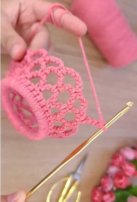 someone is crocheting an object with pink yarn and gold scissors on the table