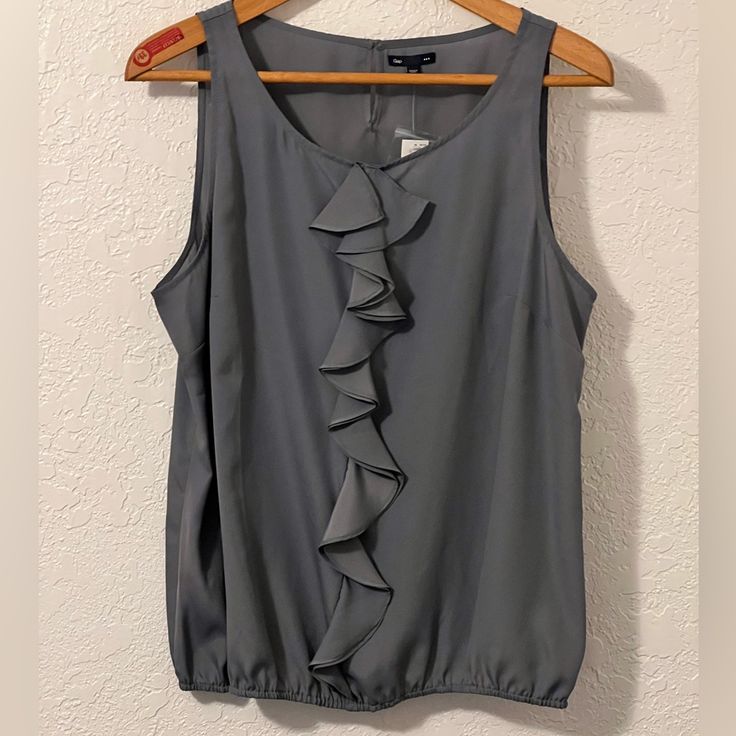 Women��’s Sleeveless Blouse From Gap. Nwt Xxl But Fits More Like And Xl. Would Look Great Under A Blazer. Ruffles Down The Front And Elastic On The Bottom Armpit To Armpit 23” Length 26” Gray Gap Ruffled Tops For Summer, Summer Ruffled Tops By Gap, Summer Ruffled Tops From Gap, Spring Gap Cami Tops, Gap Spring Cami Tops, Gap Cami Tops For Spring, Chic Sleeveless Tops By Gap, Chic Sleeveless Gap Tops, Gap Sleeveless Summer Camisole