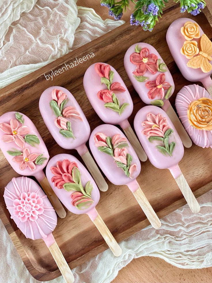 there are many pink lollipops with flowers on them sitting on a wooden tray