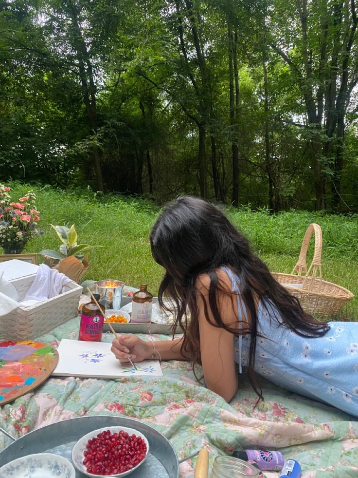 a woman laying on top of a blanket next to a table filled with food and drinks