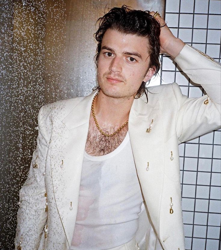 a man in a white suit standing next to a tiled wall with his hands on his head