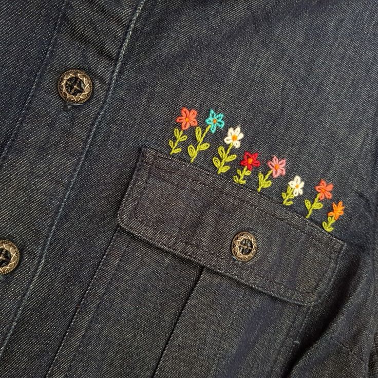 a denim shirt with embroidered flowers on the chest and buttons down the front, along with an iron - on applique