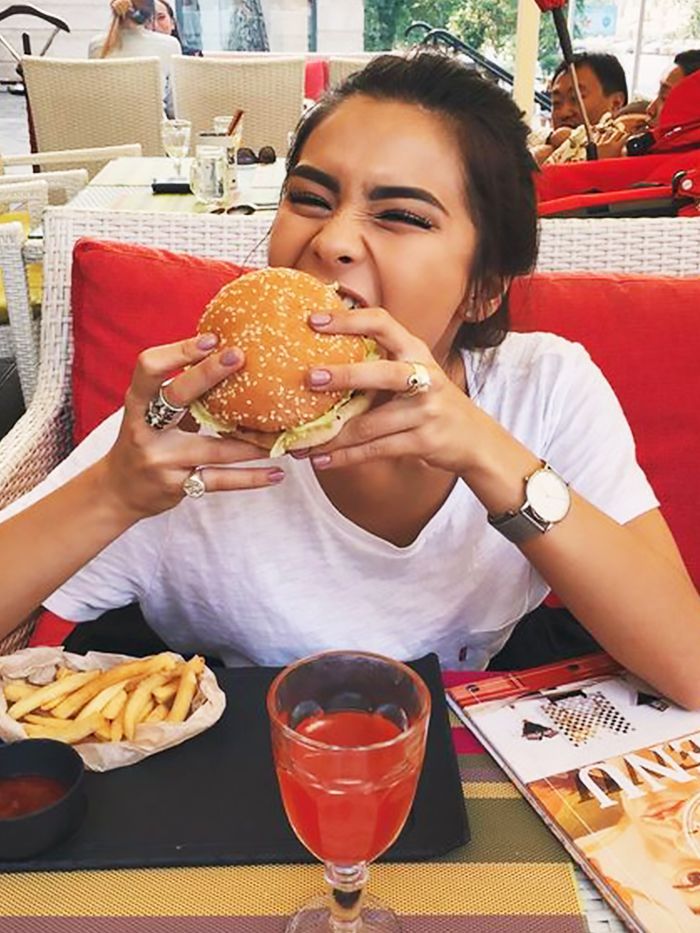 a woman sitting at a table eating a hamburger