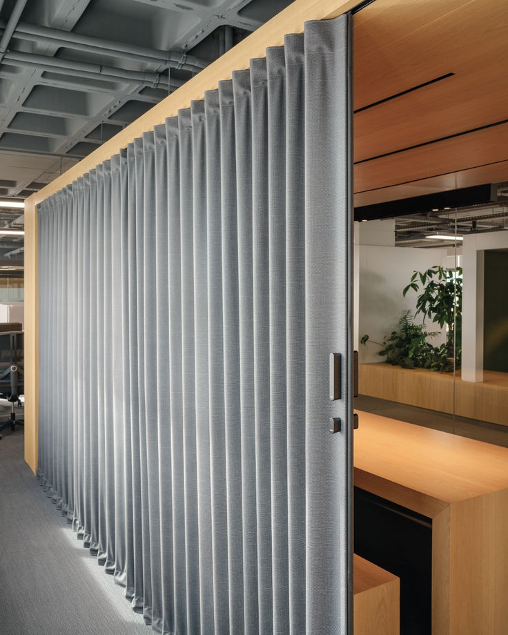 an office cubicle with vertical blinds and wooden desks