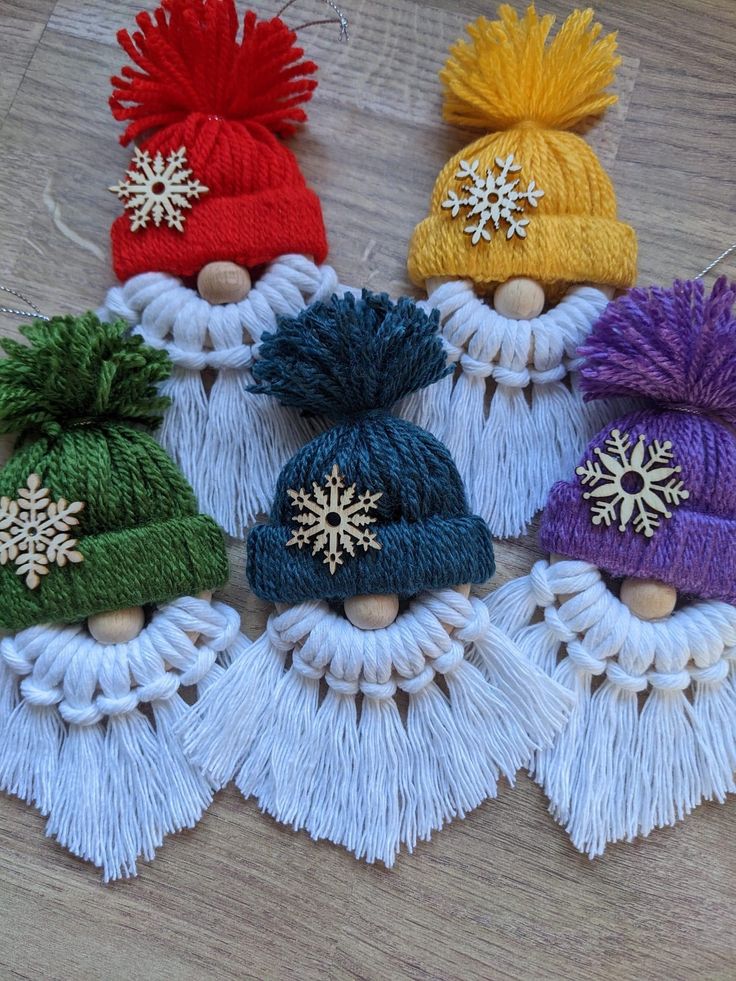 four knitted hats with tassels and snowflakes hanging from strings on a wooden surface