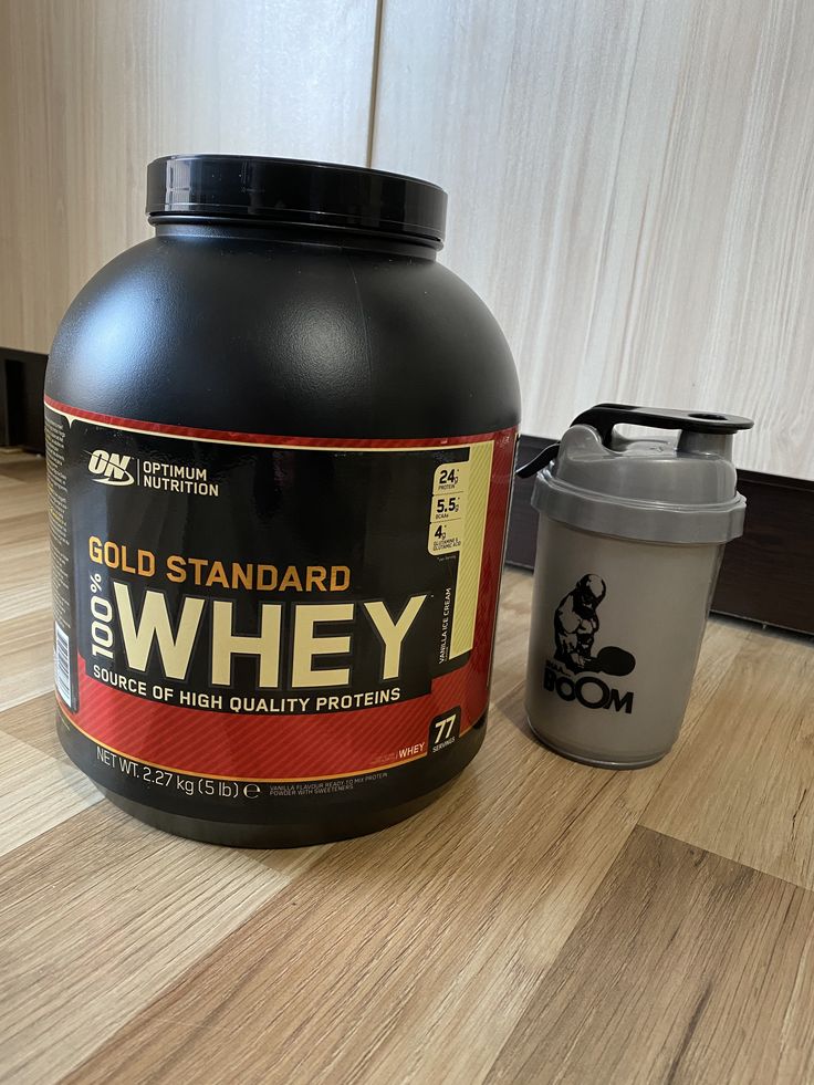 a bottle of gold standard whey next to a shaker on a wooden table