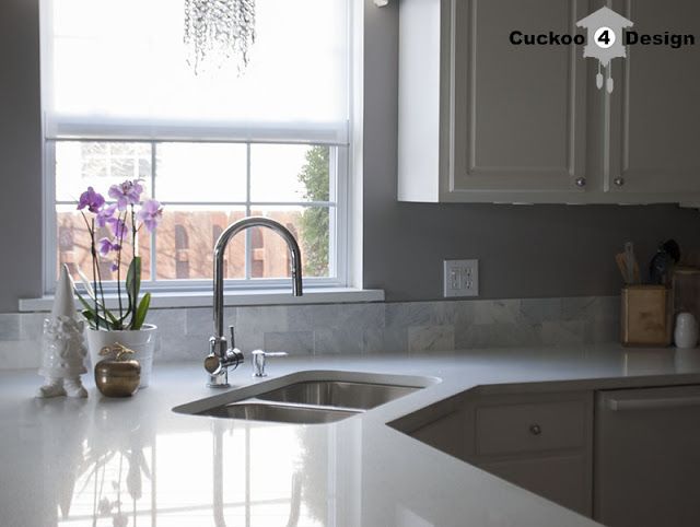 a white kitchen counter top under a window with flowers in the vase next to it