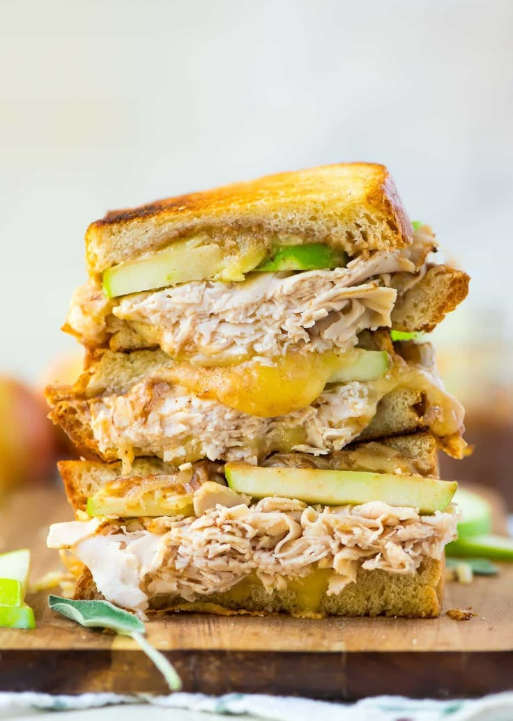 three sandwiches stacked on top of each other with meat, cheese and apples in the background