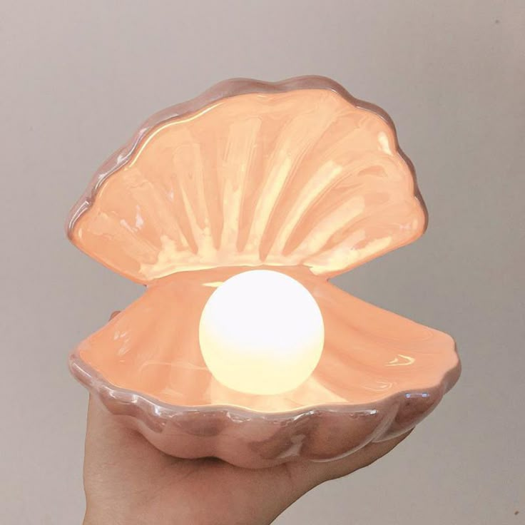 a hand holding an orange shell shaped bowl with a white light in the middle, on a gray background