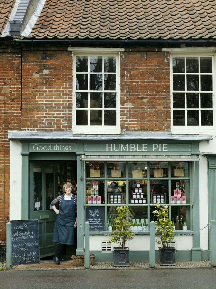 a woman standing in front of a store on the side of a road next to a brick building