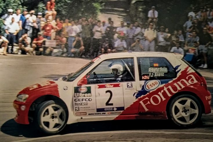 a red and white car driving down a street with people watching from the sidelines