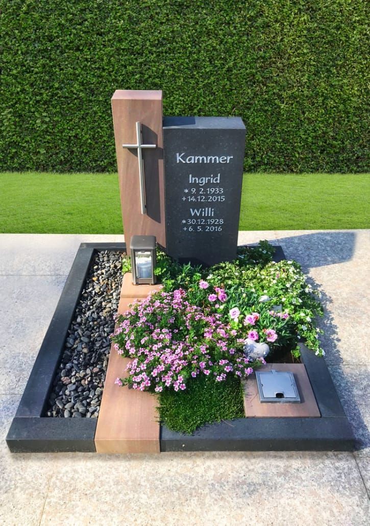 a grave surrounded by flowers and rocks in front of a green hedge with a cell phone on it