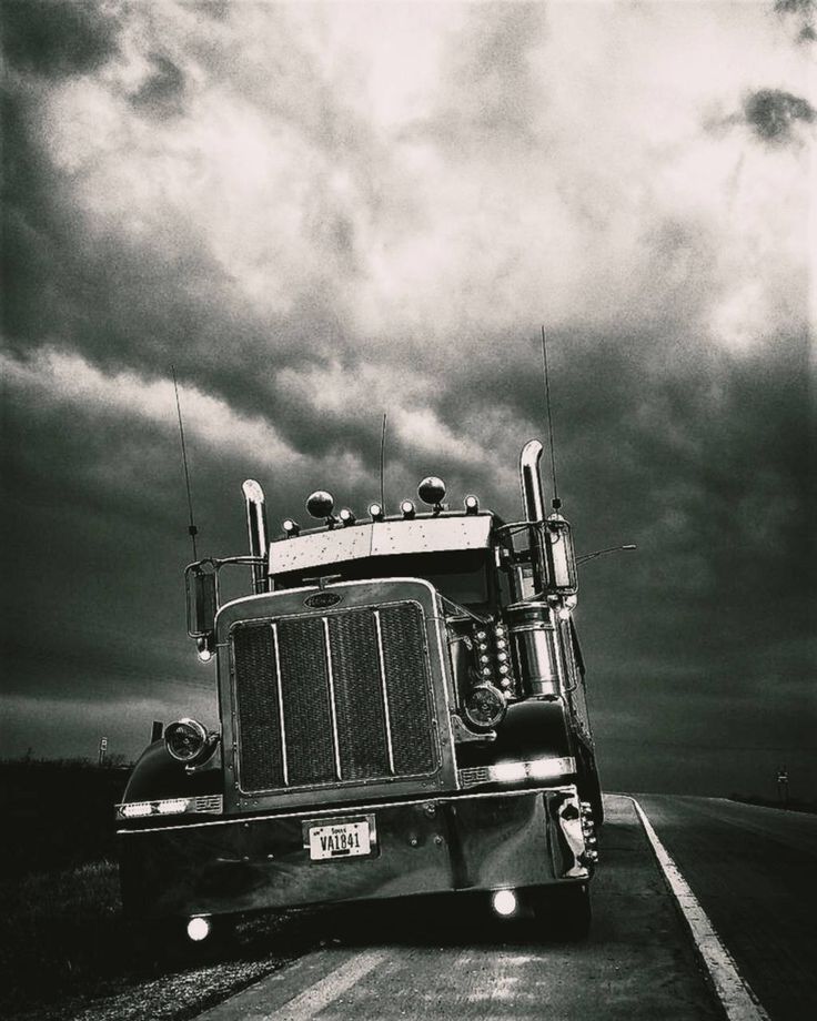 black and white photograph of a semi truck driving down the road with dark clouds in the background