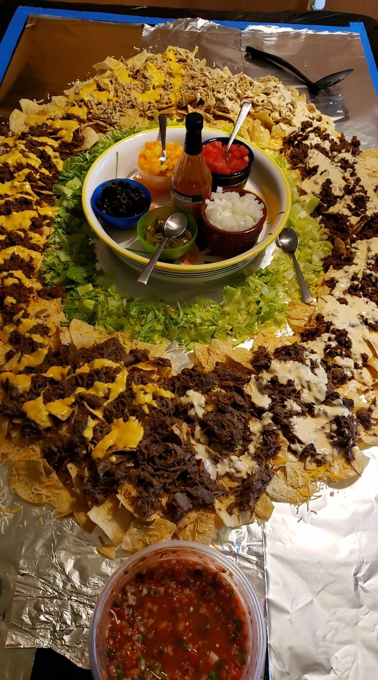 a large platter filled with lots of food on top of aluminum foil next to a bowl of salsa