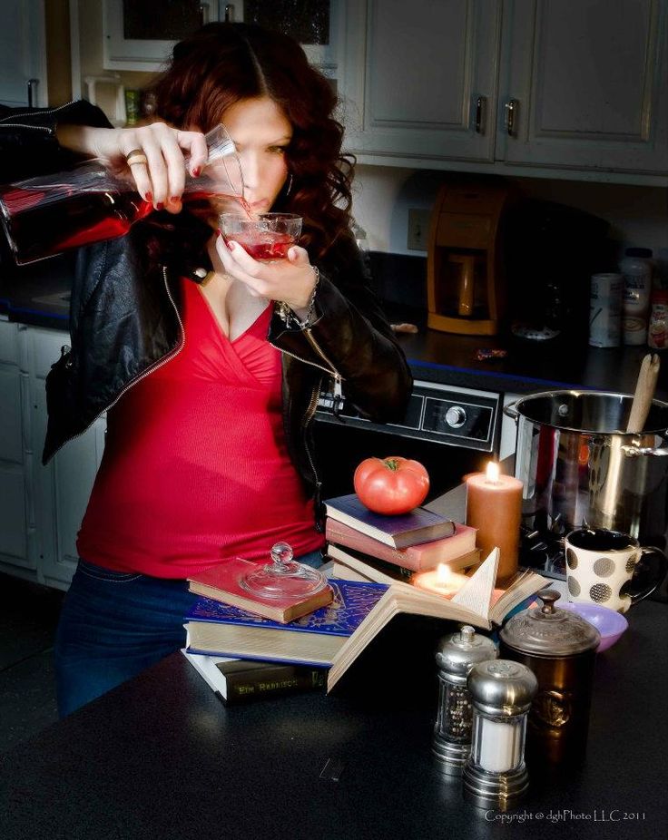 a woman in a red shirt is drinking from a wine glass while sitting at a kitchen counter