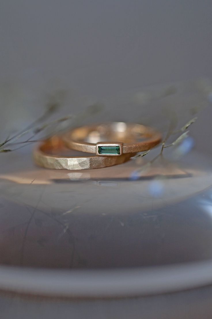 two gold wedding bands sitting on top of each other with a green stone in the middle