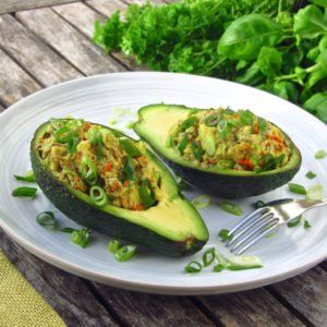 two stuffed avocados on a white plate with a fork next to them and some greens