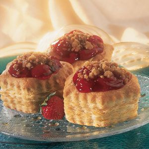 three small pastries sitting on top of a glass platter with strawberries in the middle