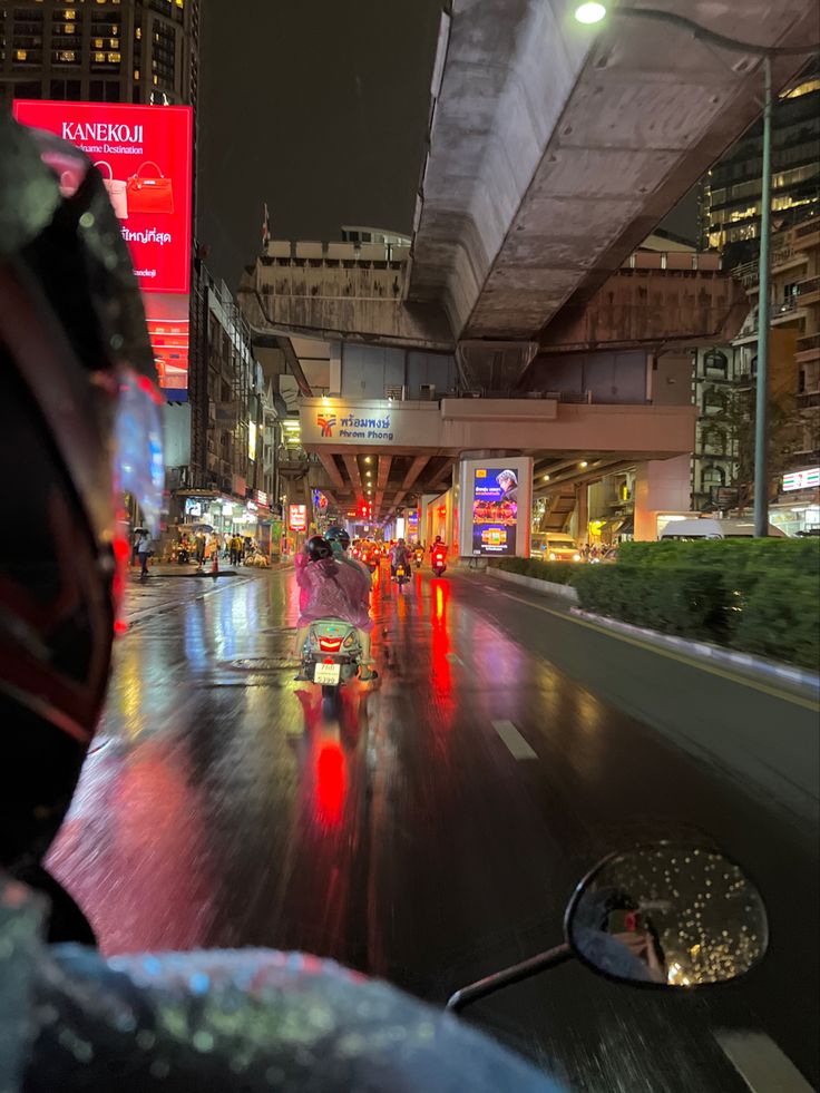 a person riding a motorcycle on a city street at night with lights reflecting off the wet pavement