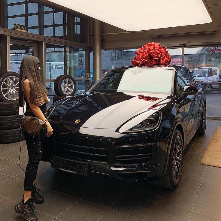 a woman standing next to a black car with a red bow on top