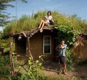 two people are sitting on the roof of a small house with grass growing on it