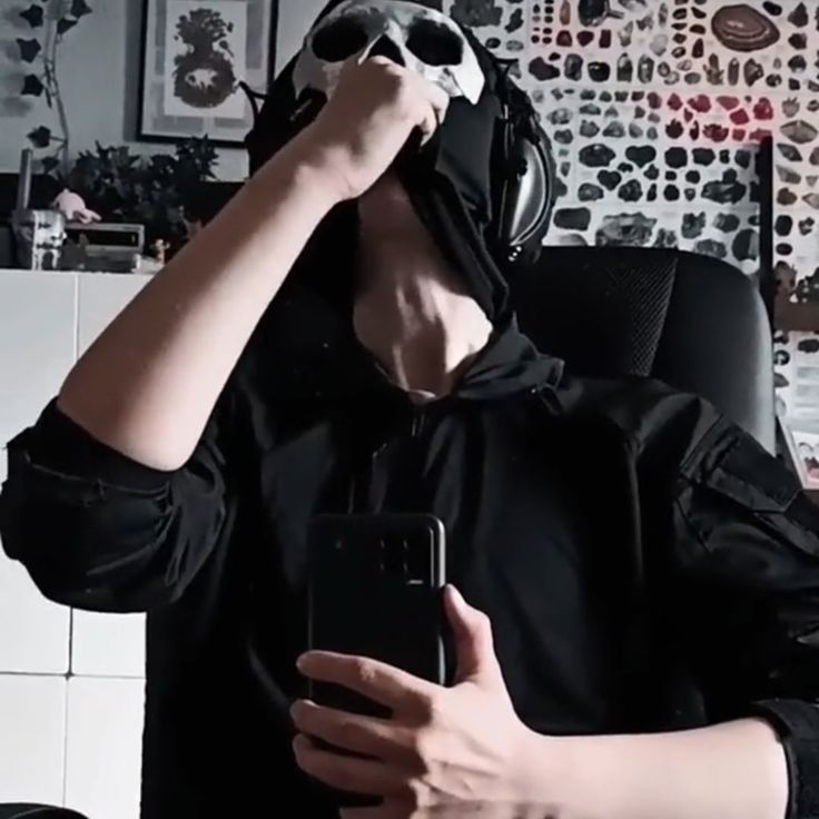 a man in a black hoodie is holding his cell phone up to his face