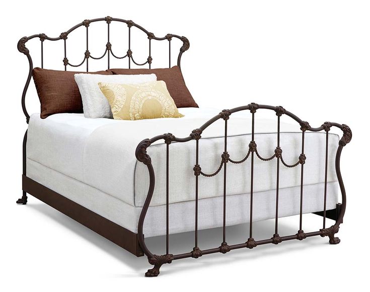 a metal bed with white sheets and brown pillows