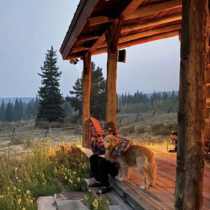 a person sitting on a porch with a dog next to them and the sun is setting