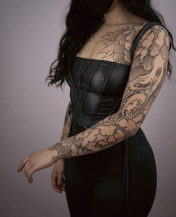 a woman with tattoos on her arms and arm sleeve is posing for the camera while wearing a black corset