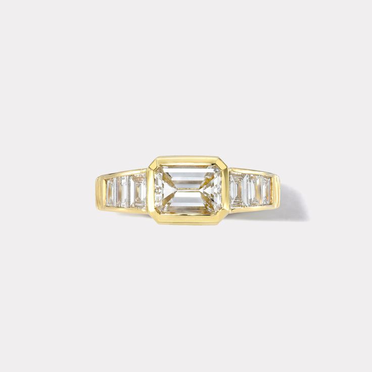 a yellow gold ring with an emerald and baguette cut diamond in the center