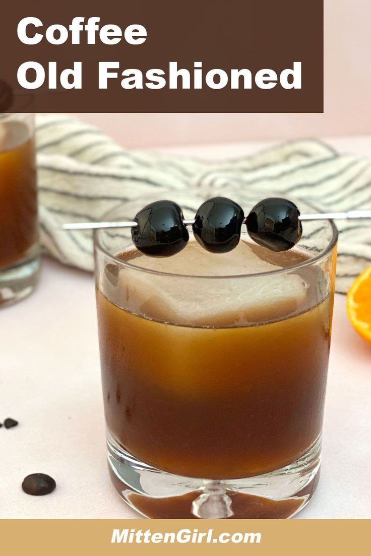 two glasses filled with coffee and black olives on top of a white table next to an orange slice