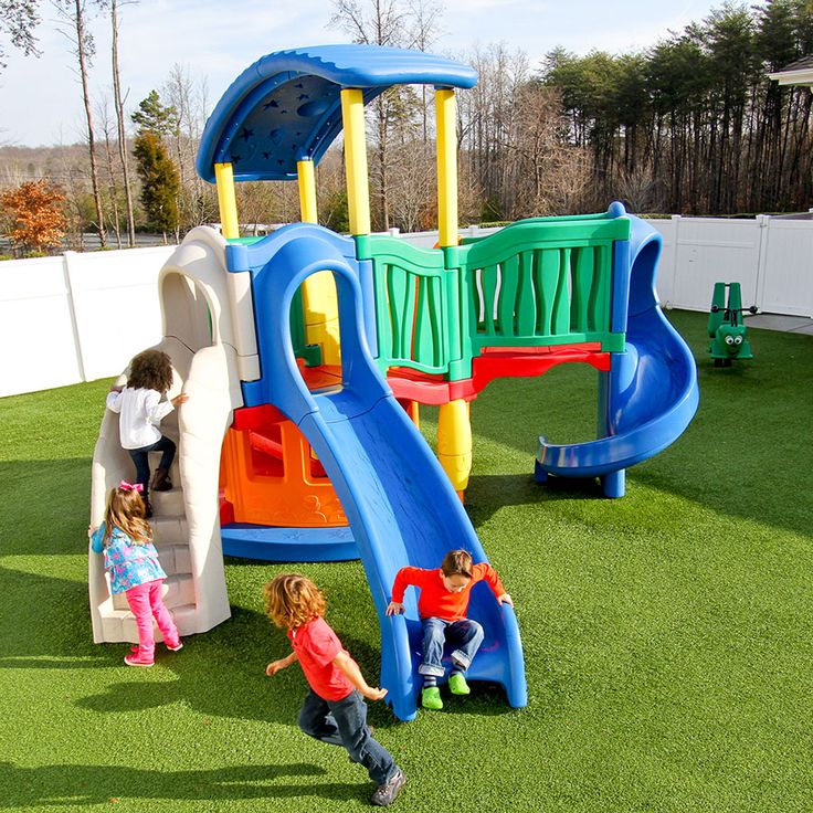 two children playing in the grass at a play ground with a slide and climbing wall