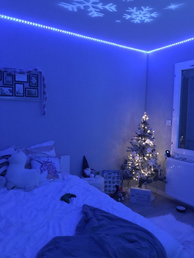 a bedroom decorated for christmas with blue lights on the ceiling and a small tree in the corner