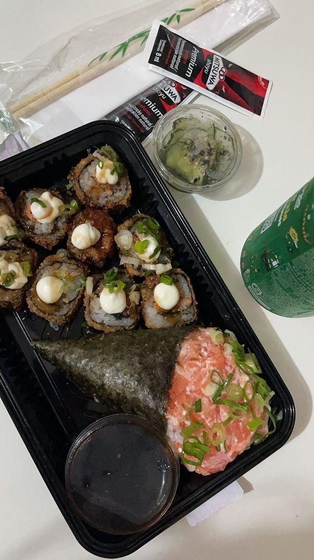 sushi and chopsticks are sitting on a black tray next to a green drink